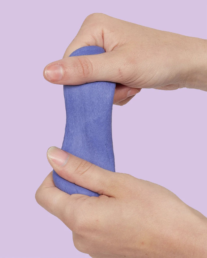 Hands stretching purple SPEKS Blur calming focus putty against a lilac background — Adventure Awaits
