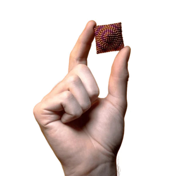 Hand holding a tiny cube of Speks rare earth fidget magnets in purple and orange - compact desk toy for adults - Adventure Awaits