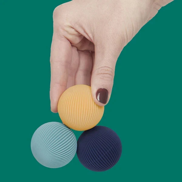 Hand holding three textured balls against a green background