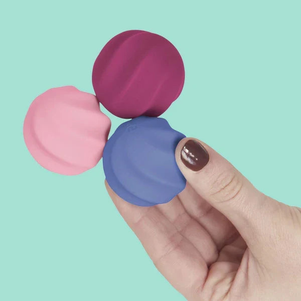 Hand holding three colorful lip balm containers against a teal background