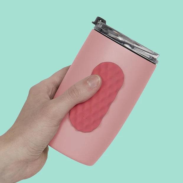 Hand holding a pink tumbler with a red silicone fidget sticker against a light blue background