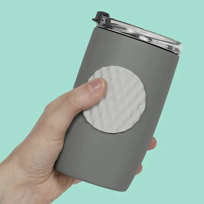 Hand holding a grey tumbler with a white circular fidget sticker by speks on a light blue background
