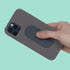 Hand holding a gray phone case with a speks slabs silicone fidget sticker on a teal background