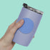 Hand holding a purple tumbler with a blue silicone speks fidget sticker against a teal background