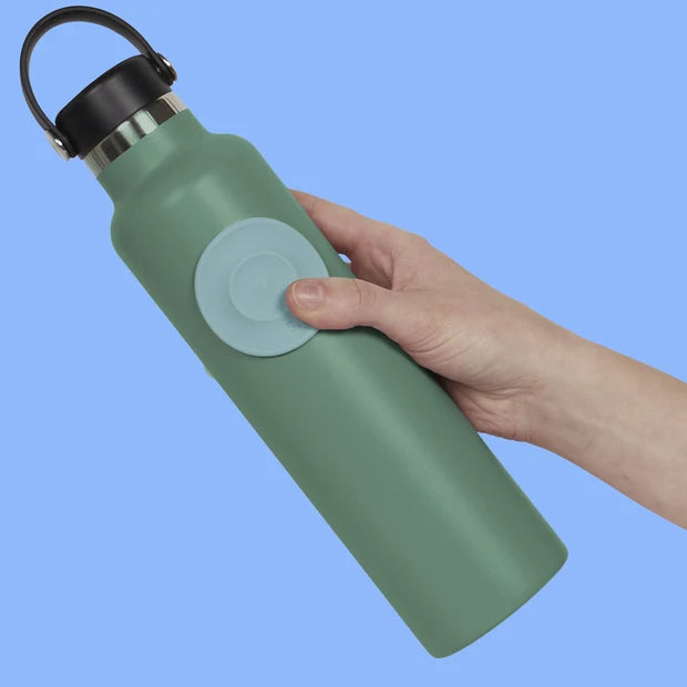 Hand holding a green water bottle with speks path fidget sticker and a black cap against a blue background