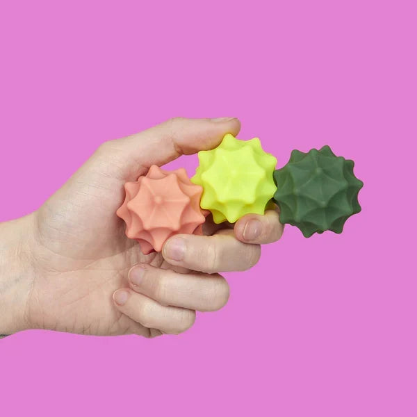 Hand holding three textured stress balls against a pink background