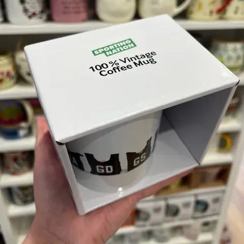 Sporting Nation vintage netball bib coffee mug in white gift box, held in a shop — Adventure Awaits
