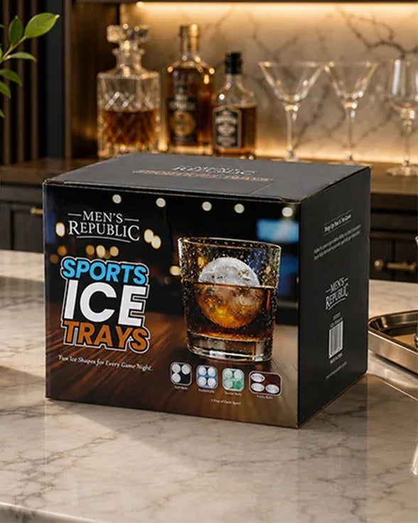A black product box for Men's Republic Sports Ice Trays sits on a marble countertop with a blurred bar scene in the background. The box features a photo of an ice cube melting in an amber drink and colorful text reading 'SPORTS ICE TRAYS'.