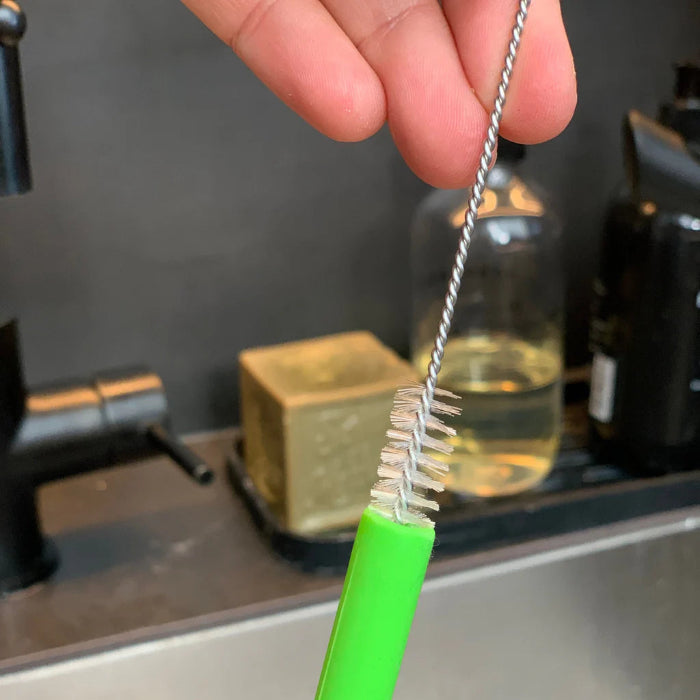 Cleaning brush inside bright green reusable straw at kitchen sink — Adventure Awaits