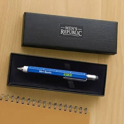 A blue and silver mechanical pencil with a ruler scale design and 'Men's Republic' branding, displayed inside its black presentation box on a light wood tabletop next to a spiral notebook.