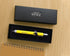 A yellow and silver Men's Republic branded retractable pen with a measuring scale design, presented in an open black gift box on a light wood tabletop.