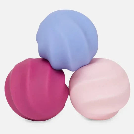 Three silicone sensory balls in pastel purple, magenta pink, and light pink, arranged in a pyramid on a light gray background.