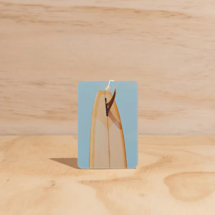 The Commonfolk Mustard Tail Surfboard boho hanging air freshener with Byron Bay scent of almond milk & coconut milk on a light timber background — Adventure Awaits