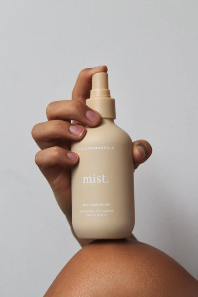 Hand holds The Commonfolk Mist body, linen and room spray in soft peach bottle with almond milk & coconut milk scent — Adventure Awaits