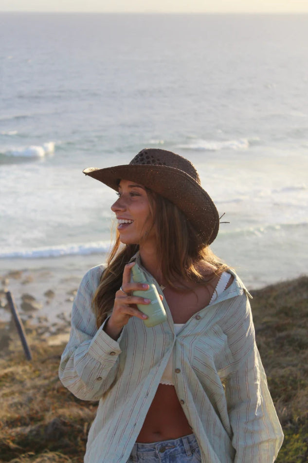 Woman smiling holding The Commonfolk Mist body, linen and room spray in sage green with cucumber mint scent — Adventure Awaits