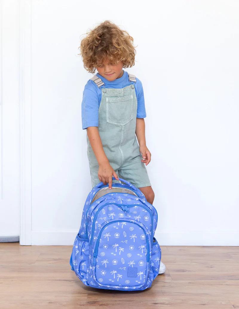 Child holding a blue backpack with airplane pattern on a wooden floor.