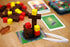 Colorful building block tower on a wooden surface with cards and a small tool.