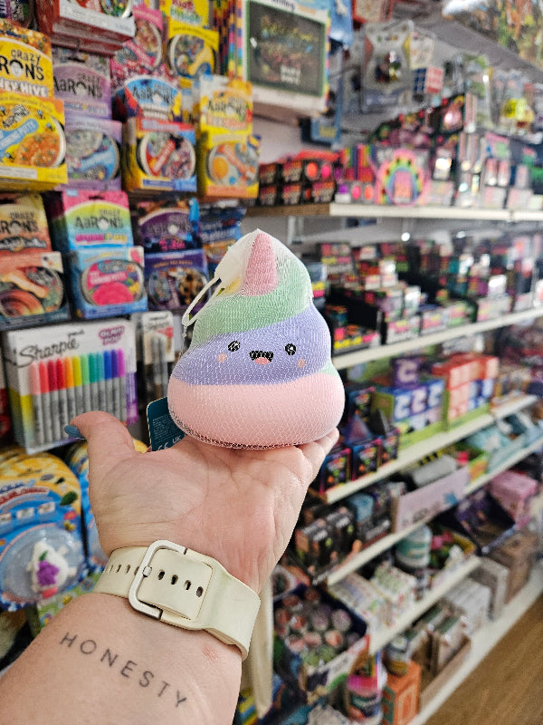 Hand holding a small plush toy with a colorful background of books and stationery items.