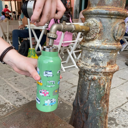 Person filling a green water bottle with a camper design from a public water fountain.