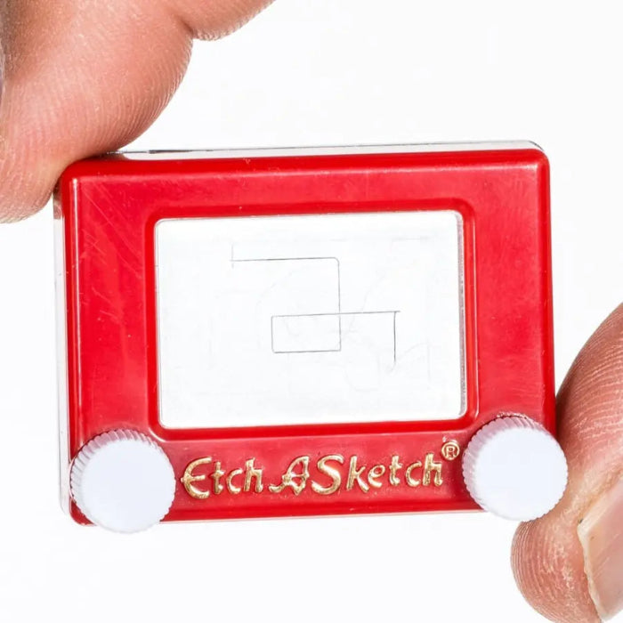 Tiny red Etch A Sketch drawing toy held between fingers with white knobs — Adventure Awaits