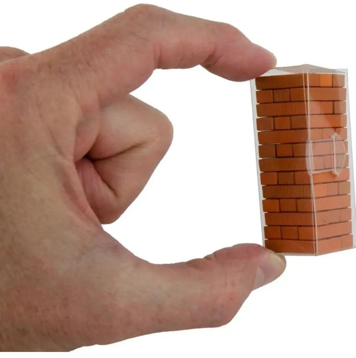 Hand holding a tiny wooden brick stacking tower game in a clear storage case — Adventure Awaits