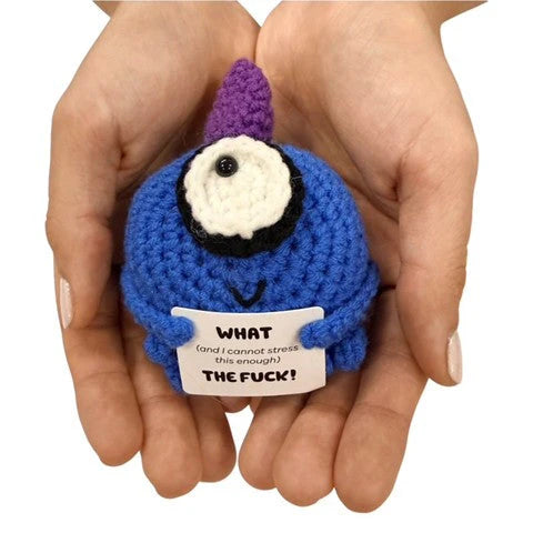 hands holding a handmade crochet blue cyclops plush toy with a humorous sarcastic quote sign