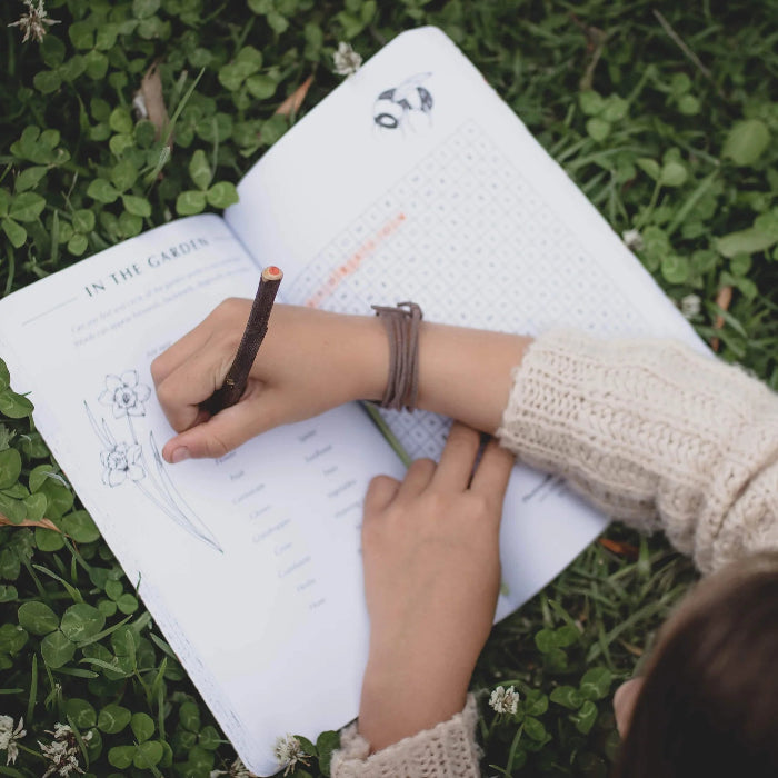 Child completing an outdoor garden activity in the Wild Activity Book while sitting on grass — Adventure Awaits