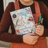Child holding Wild Activity Book and colourful markers for screen-free nature activities — Adventure Awaits