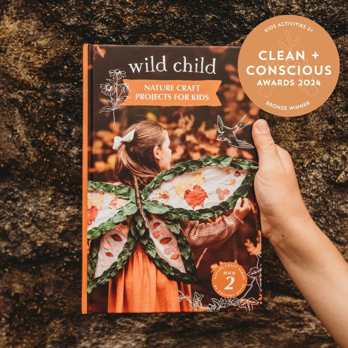 Hand holding Wild Child Nature Craft Projects for Kids book outdoors with award badge — Adventure Awaits