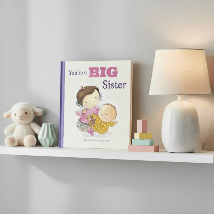 Adventure Awaits You’re a Big Sister children’s book displayed on a nursery shelf beside a lamp and plush toy