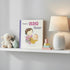 Adventure Awaits You’re a Big Sister children’s book displayed on a nursery shelf beside a lamp and plush toy