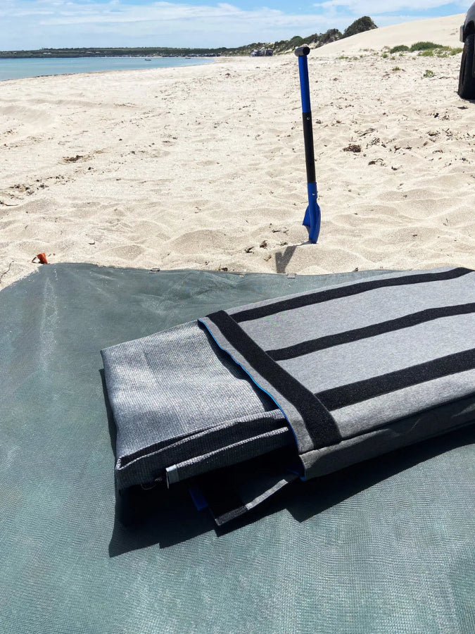 Navigator grey caravan storage bag folded on beach mat beside sand and shovel — Adventure Awaits