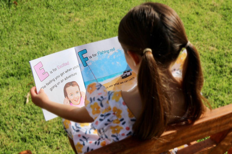 child sitting outdoors reading ABC for Little Offroaders book, learning letters with colourful adventure themed pages on grass Adventure Awaits