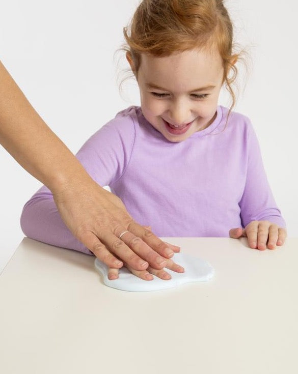 girl in purple shirt making handprint in white clay with adult hand helping her make impression