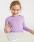 girl in purple shirt sitting behind handprint impression made on white clay 