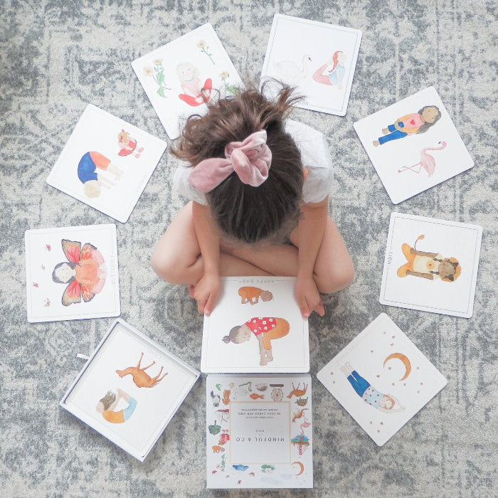 Child sitting among Mindful & Co yoga cards, choosing an illustrated mindfulness activity — Adventure Awaits