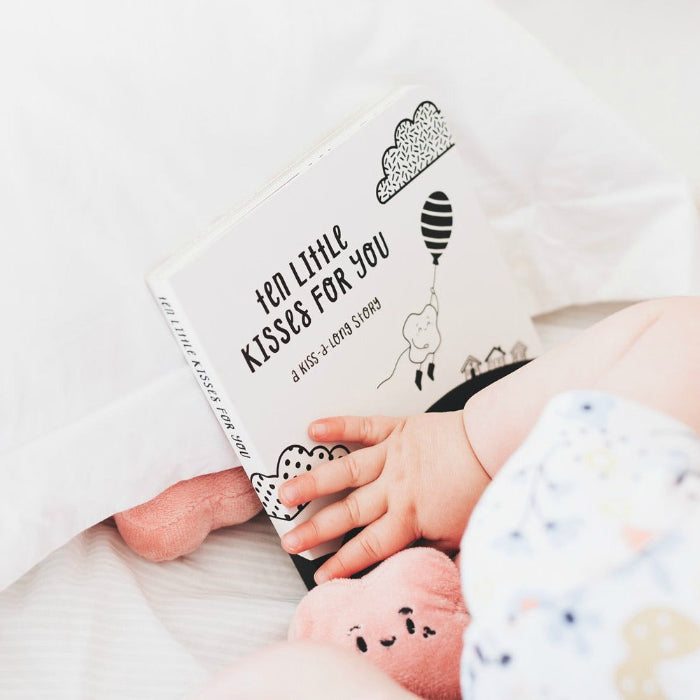 Baby reaching for Ten Little Kisses For You board book in bed — Adventure Awaits