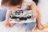 Baby looking at black and white Ten Little Kisses For You board book on bed — Adventure Awaits