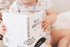 Baby holding Ten Little Kisses For You board book on soft bedding — Adventure Awaits
