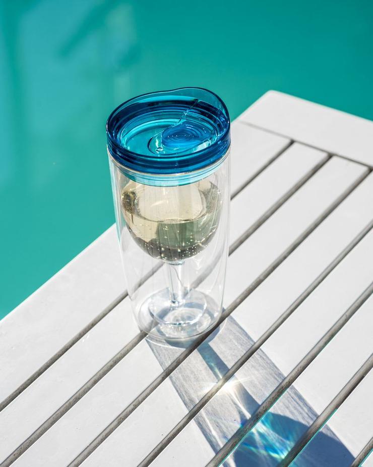 double wall wine tumbler with blue lid filled with white wine on outdoor table by pool, insulated travel drinkware for summer and outdoor use Adventure Awaits