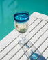 double wall wine tumbler with blue lid filled with white wine on outdoor table by pool, insulated travel drinkware for summer and outdoor use Adventure Awaits