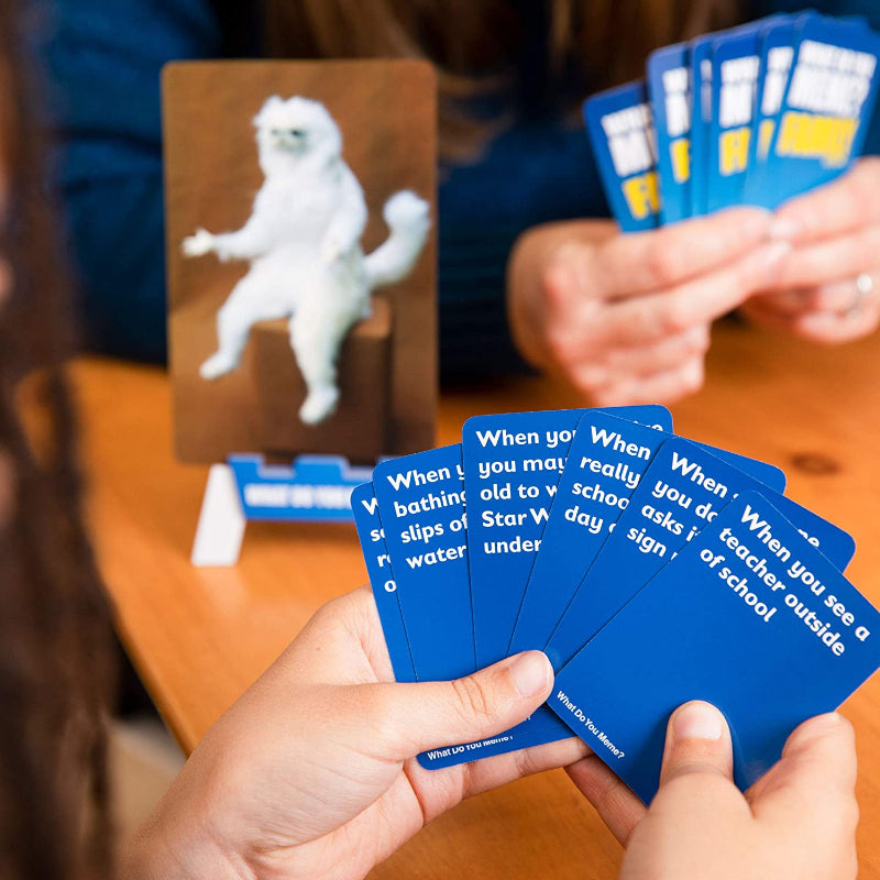 Players hold blue caption cards while playing What Do You Meme? Family Edition at a table — Adventure Awaits